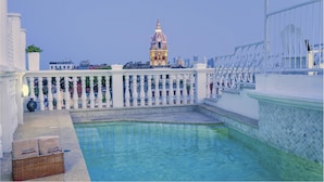 Zona de piscina con barandilla blanca, una cesta de mimbre con toallas y vista a un edificio con cúpula y aguja al fondo.