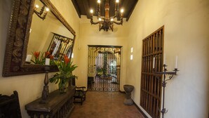 Un pasillo con un espejo grande y ornamentado, una araña y un portón que da a un patio.