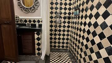 Un baño con piso y paredes a cuadros, un espejo con marco ornamentado y una zona de ducha con desagüe.