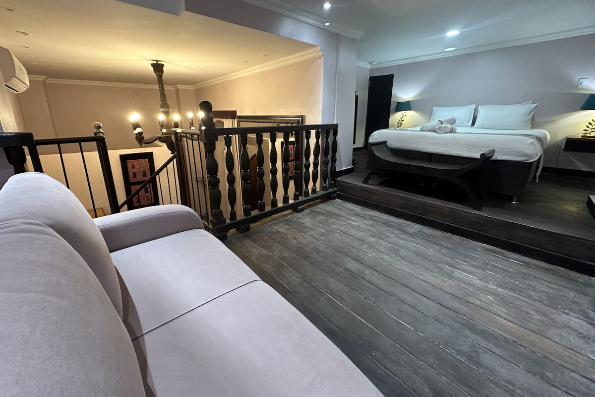 Una habitación de hotel moderna con una cama grande, un sofá y una escalera con barandilla.