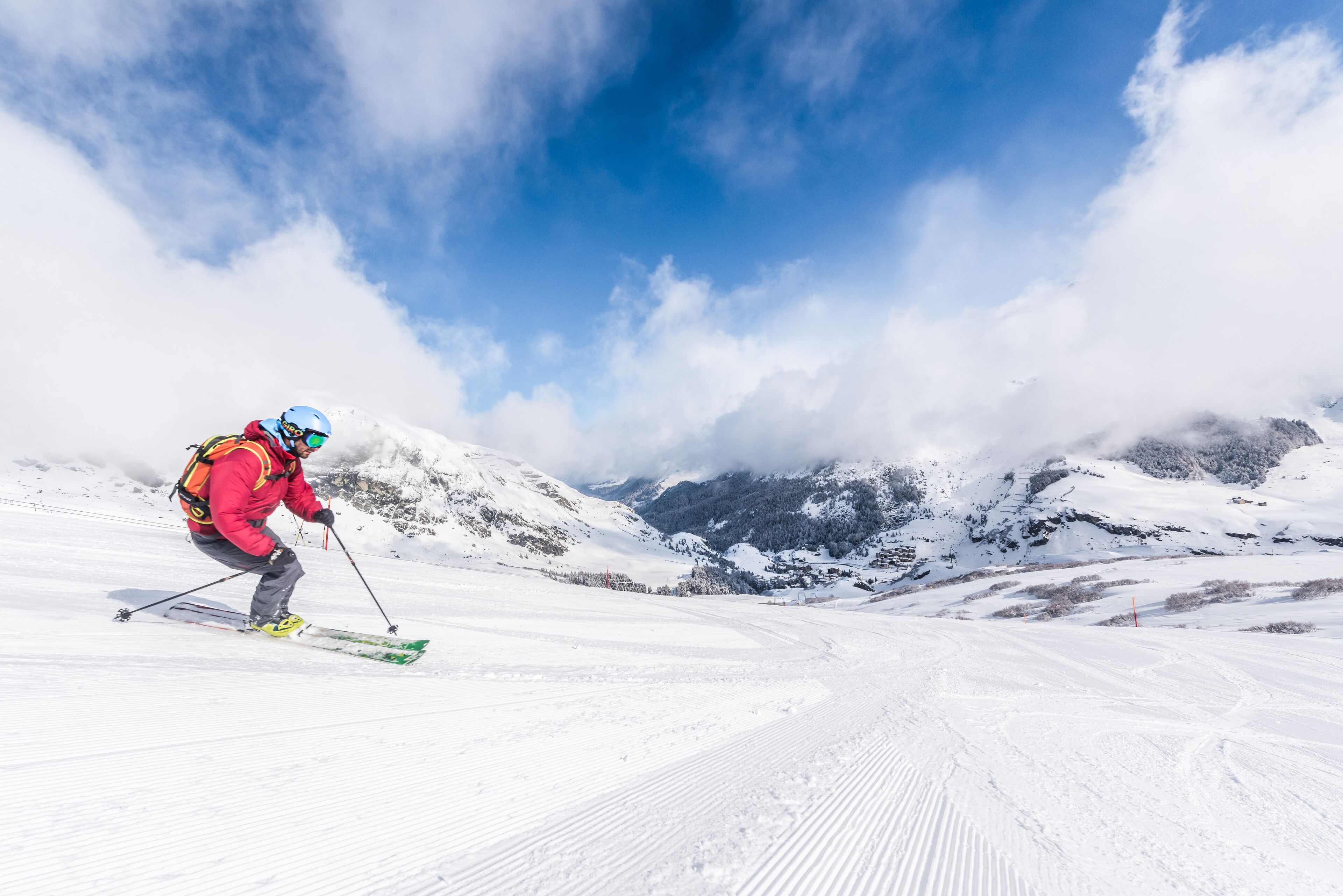 Ein Skifahrer auf einem verschneiten Hang, im Hintergrund Berge.