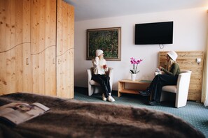 Una habitación con un armario de madera, un cuadro en la pared, un televisor y una mesita con una planta en maceta.