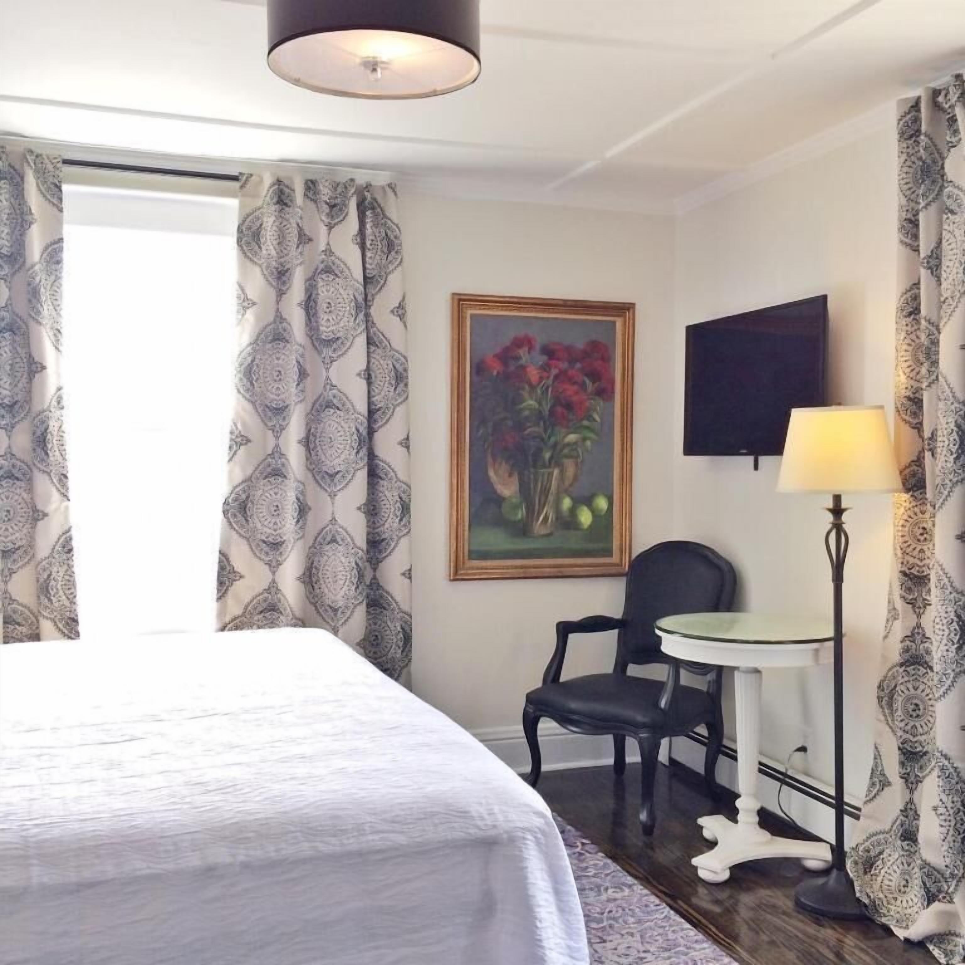 Habitación de hotel con cama, sillón, una mesita, un cuadro, televisor y cortinas estampadas.