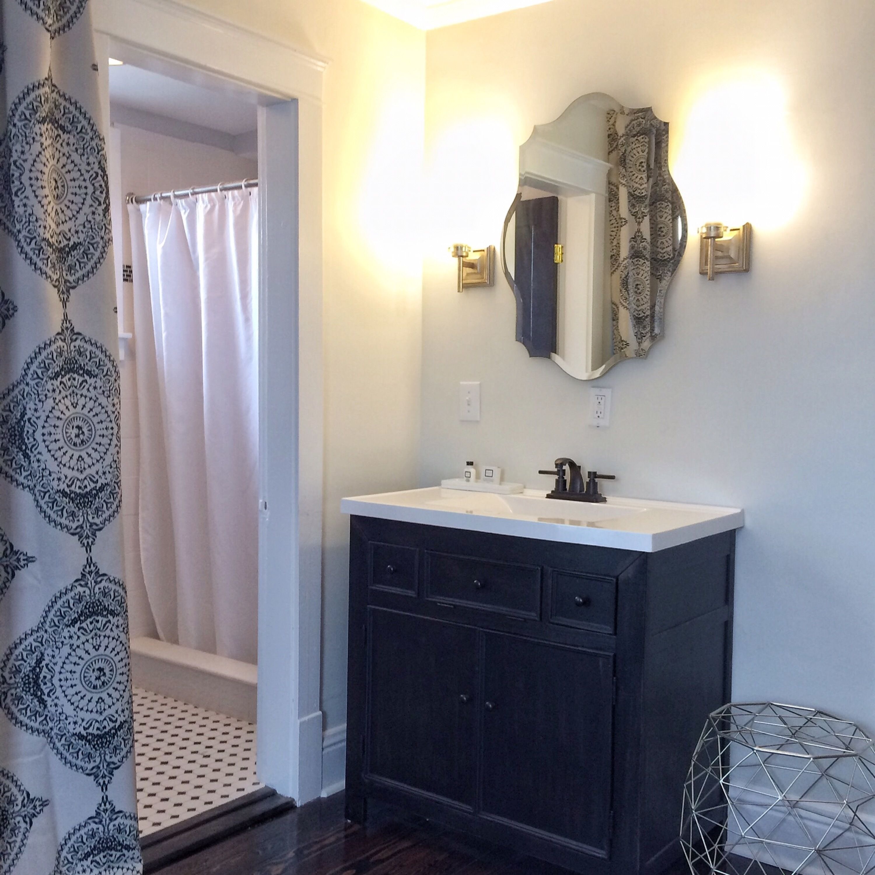 Un baño con tocador oscuro, lavamanos blanco y espejo con dos apliques de pared.