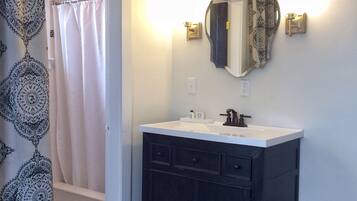 Un baño con tocador oscuro, lavamanos blanco y espejo con dos apliques de pared.