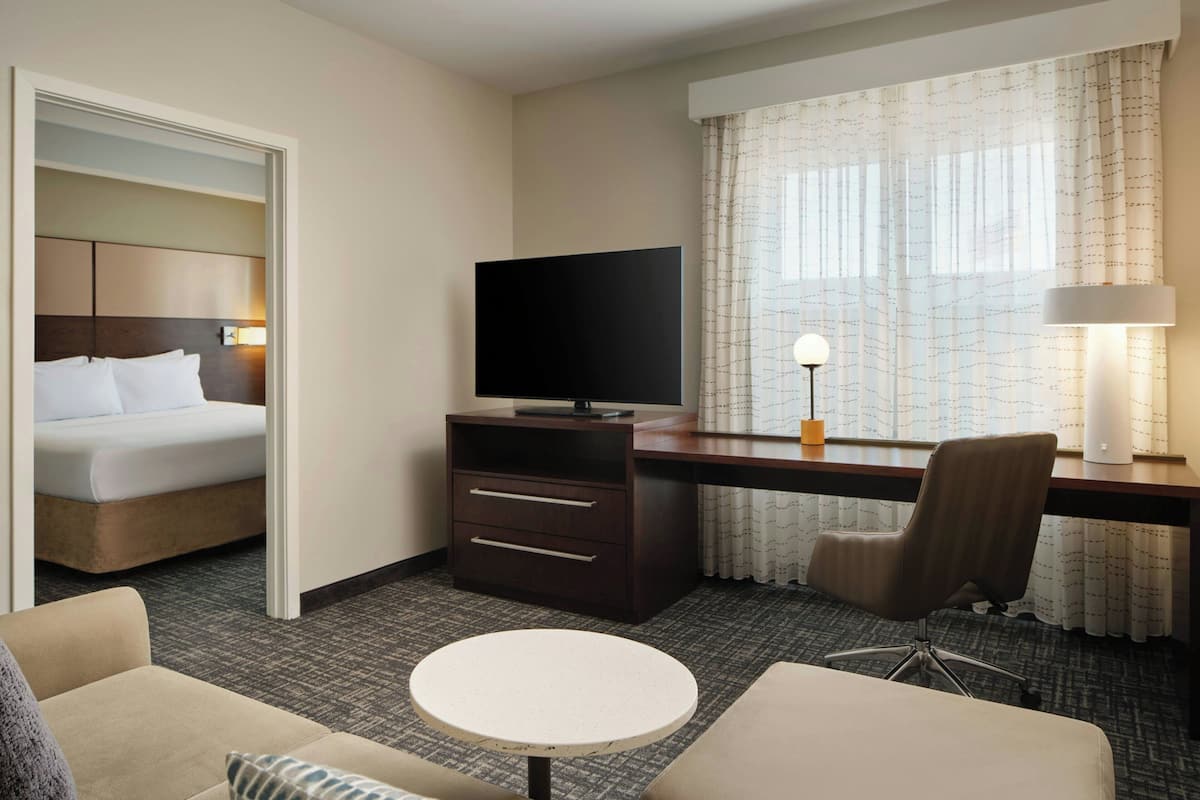 Hotelkamer met een bed, een bureau met televisie, een stoel, een klein rond tafeltje en een raam met gordijnen.