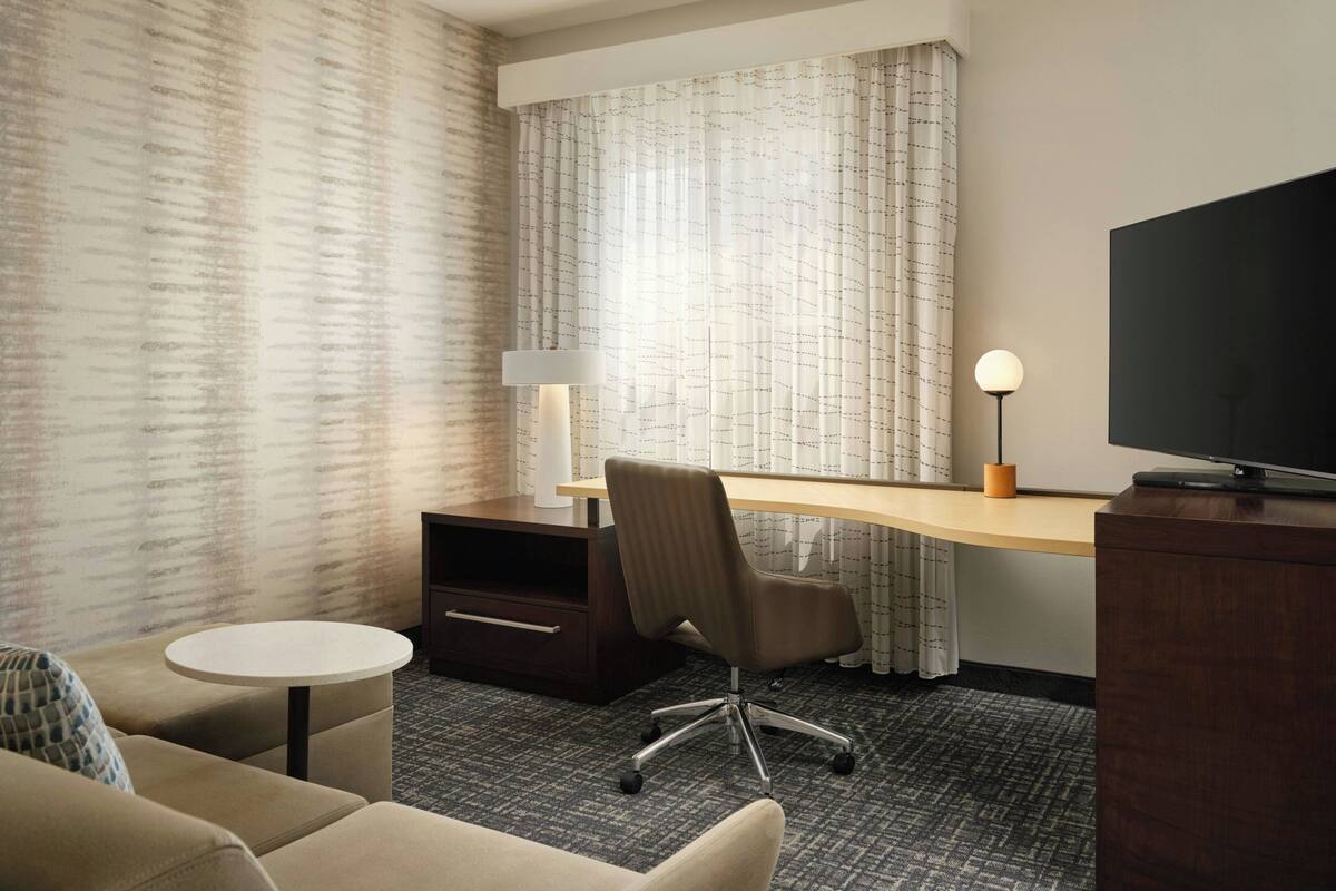 Een hotelkamer met een bureau, stoel, televisie en een klein rond tafeltje.