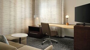 Habitación de hotel con escritorio, silla, televisor y una pequeña mesa redonda.