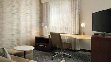 Habitación de hotel con escritorio, silla, televisor y una pequeña mesa redonda.