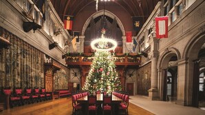 Ein prunkvoller Saal mit einem großen Weihnachtsbaum, aufwendiger Dekoration und einem langen Esstisch mit rot gepolsterten Stühlen.