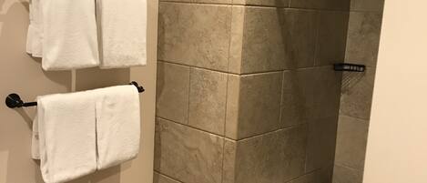 Un área de ducha con azulejos color beige, un perchero de metal y un perchero blanco.