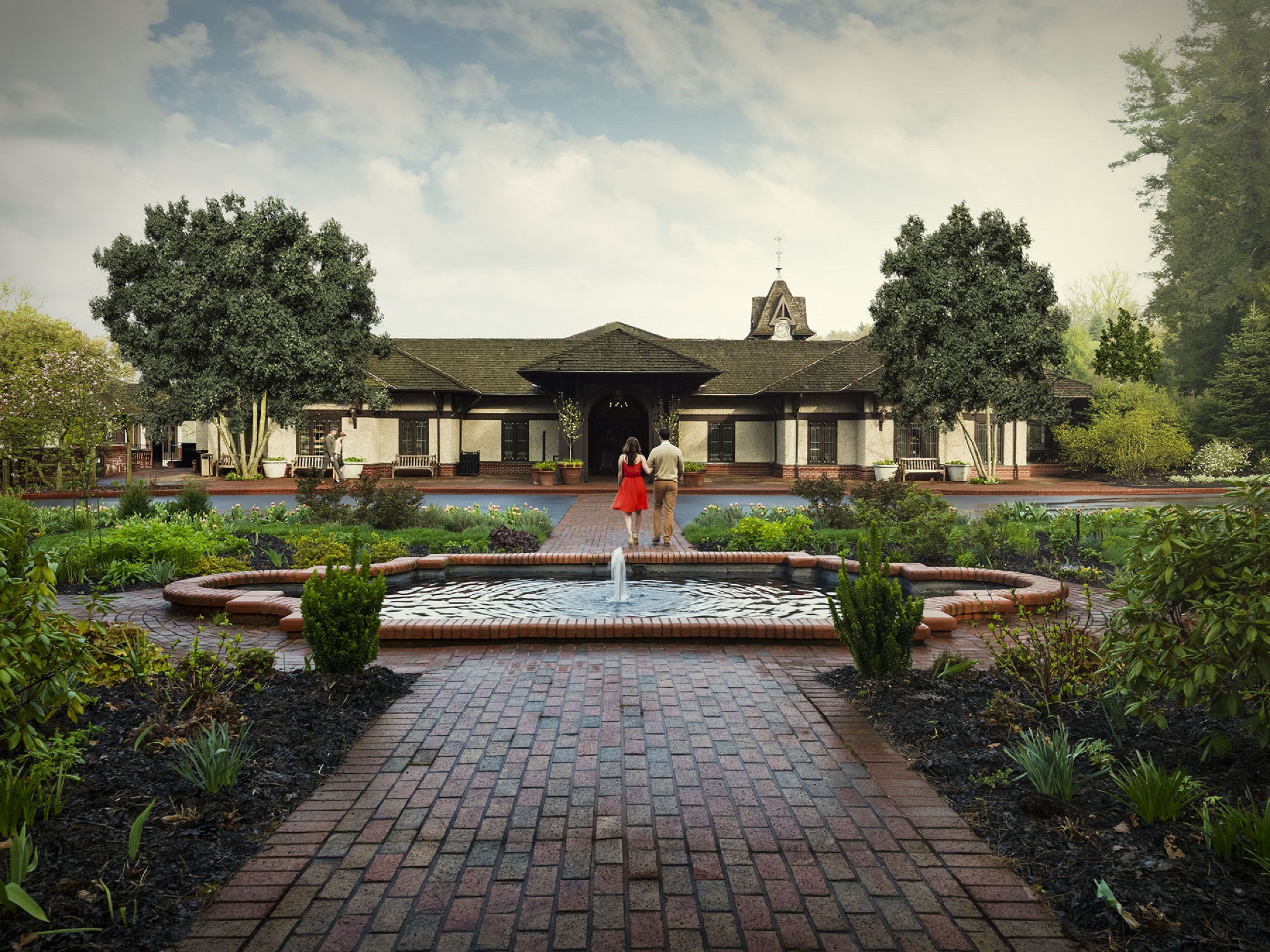A courtyard with a fountain, brick pathway, and a building with a clock tower.