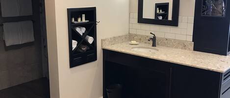 A modern bathroom with a dark vanity, a large mirror, and a tiled floor.