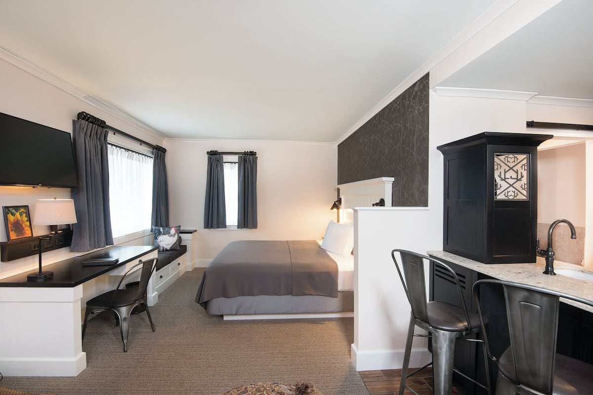Habitación de hotel compacta con cama, escritorio, silla, televisor y zona de baño.