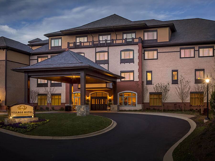 A multi-story hotel with a covered entrance, a landscaped front yard, and a sign reading "VILLAGE HOTEL."