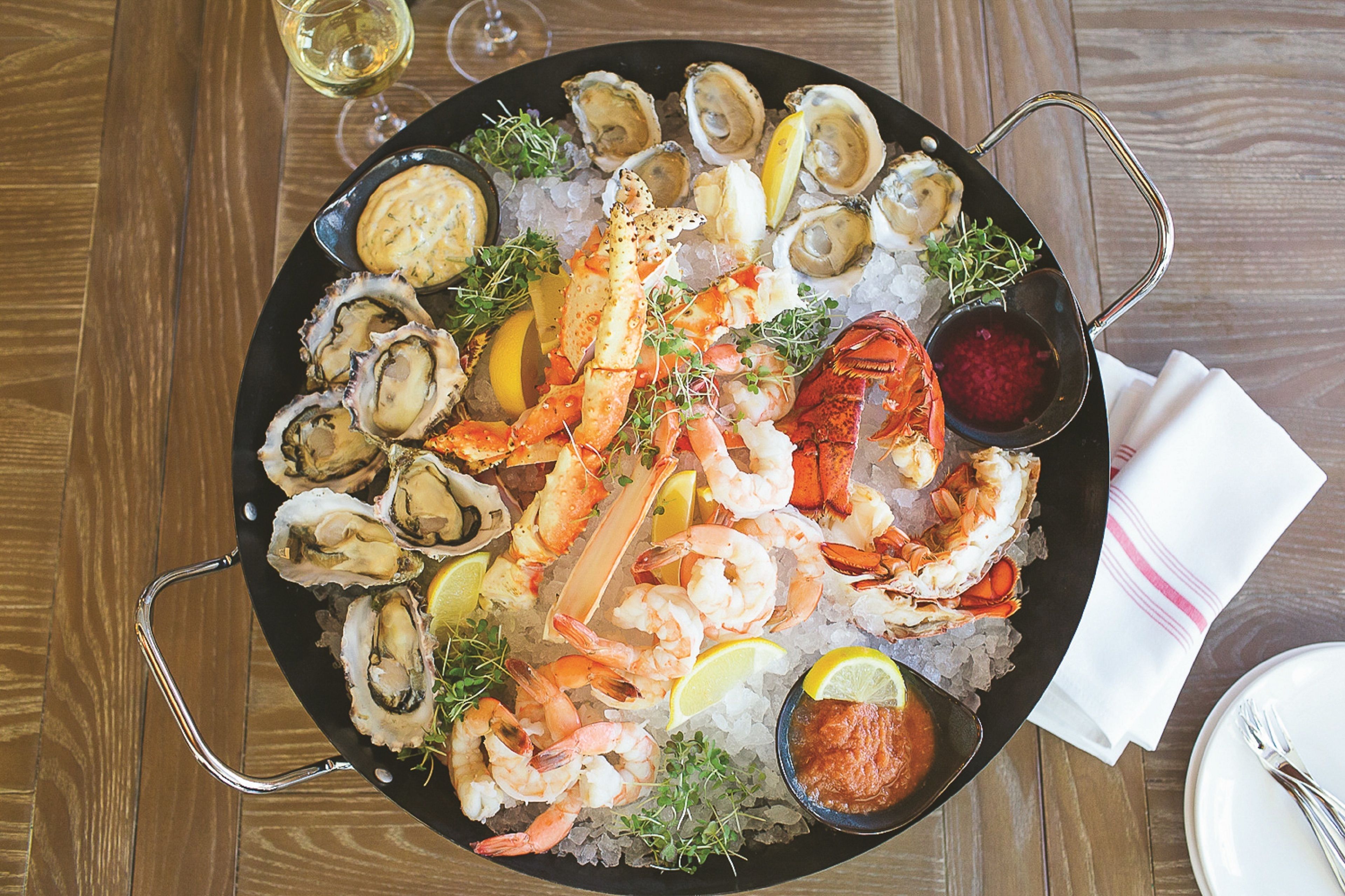 Uma seleção de frutos do mar com ostras, camarões, lagosta e caranguejo sobre gelo, acompanhada de fatias de limão e molho para acompanhar.