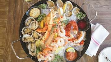 Uma seleção de frutos do mar com ostras, camarões, lagosta e caranguejo sobre gelo, acompanhada de fatias de limão e molho para acompanhar.