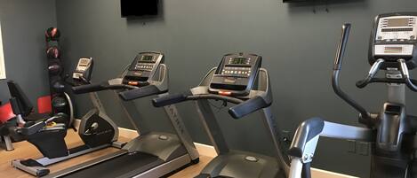 A gym with treadmills, a weight bench, and a wall-mounted TV.