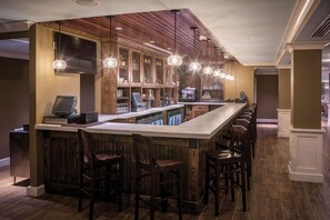 A bar area with a long counter, wooden bar stools, and pendant lighting.