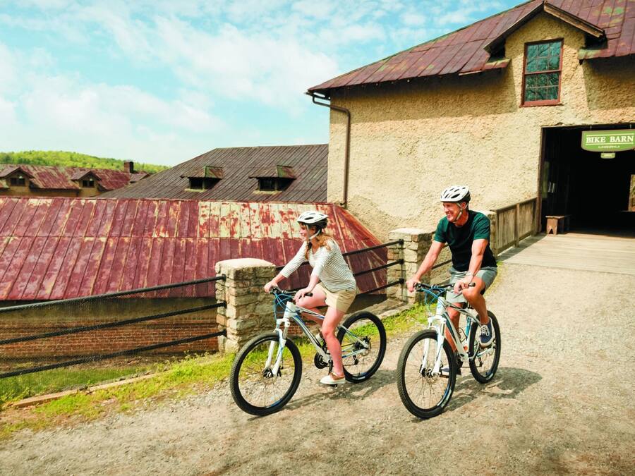 Two people riding bicycles on a path with a rustic building in the background.