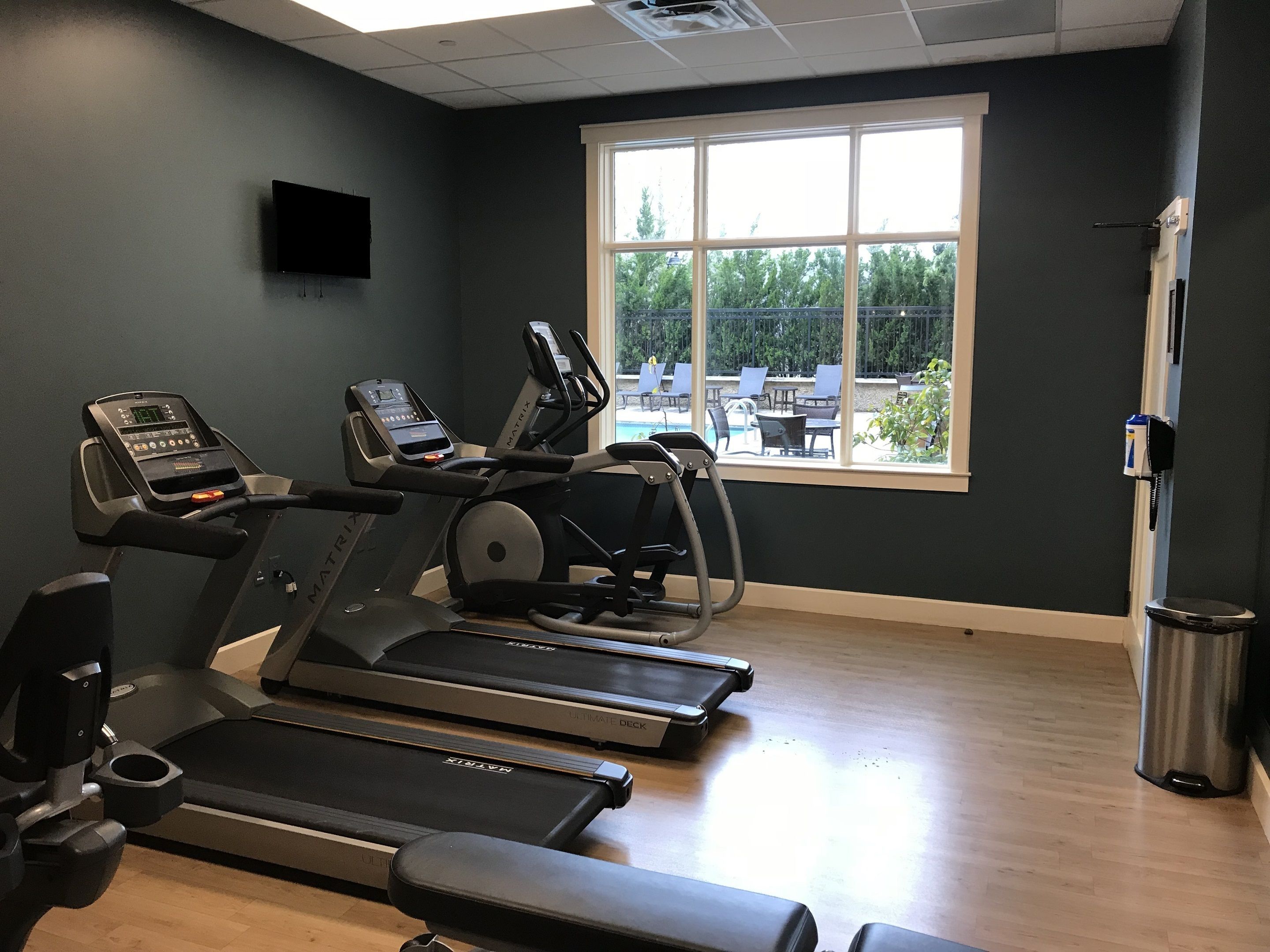 A gym with three treadmills, a stationary bike, and a wall-mounted TV.