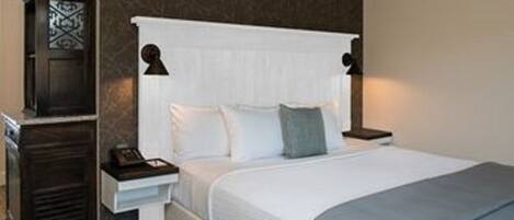A neatly made bed with a white headboard, a bedside table with a lamp, and a dark wooden nightstand.