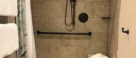 A shower area with a grab bar, a small bench, and a towel rack.