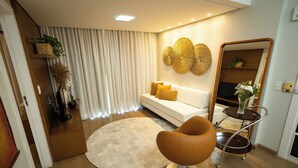 A modern living room with a white sofa, a round rug, a brown chair, and a decorative mirror. - Alfa Hotel (Vicosa)