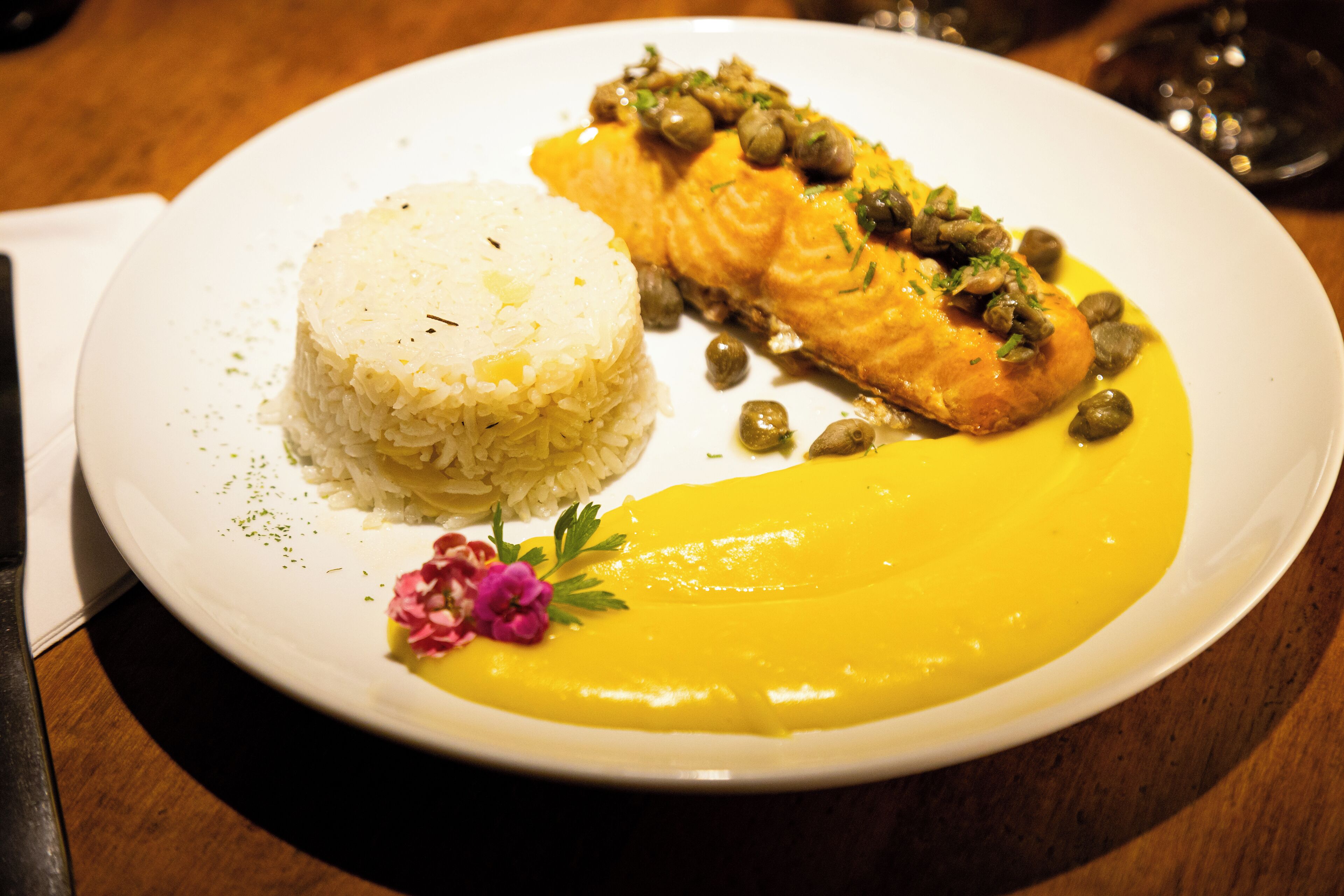 A plate with a piece of salmon, rice, and a yellow sauce.