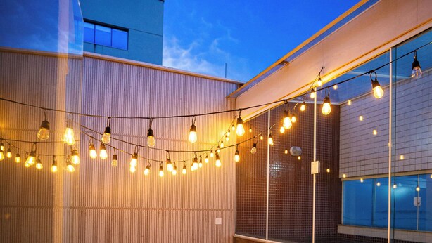 A modern outdoor patio with a dining table and chairs, string lights, and a view of the cityscape. - Alfa Hotel (Vicosa)
