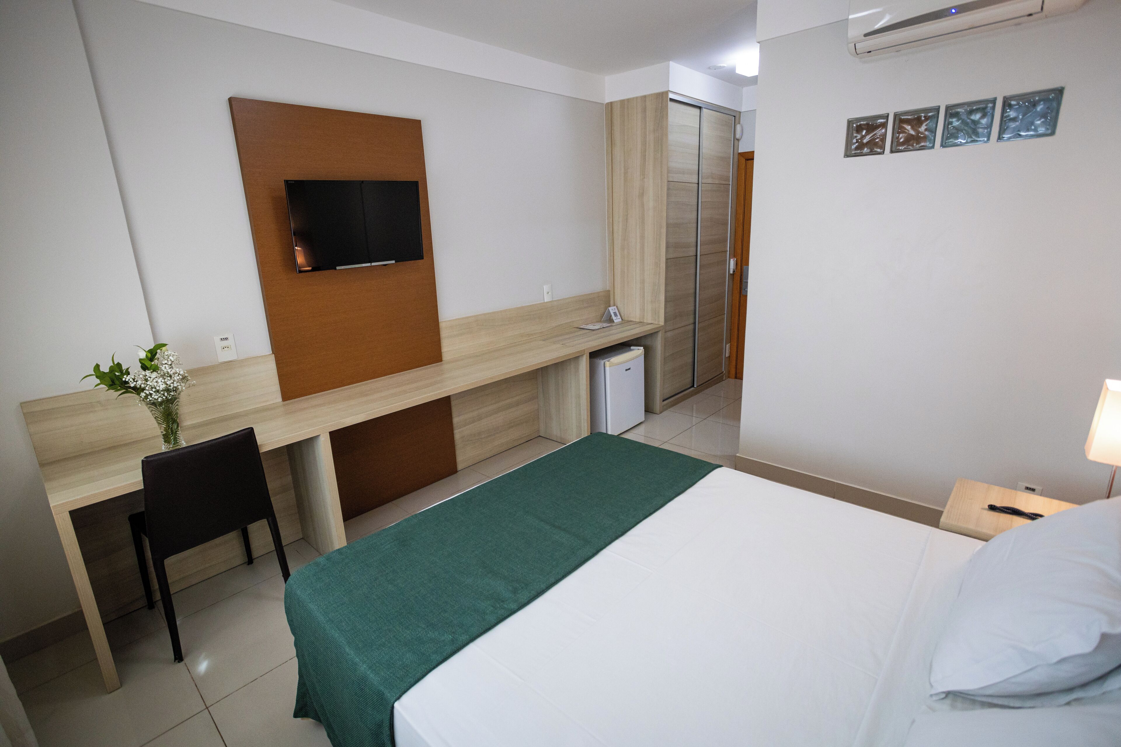 Habitación de hotel con cama, escritorio, silla, televisor montado en la pared y un mueble pequeño.