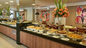 A buffet with various food items and a floral centerpiece. - Alfa Hotel (Vicosa)