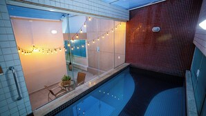 A modern indoor swimming pool with clear glass walls, string lights, and a tiled floor. - Alfa Hotel (Vicosa)