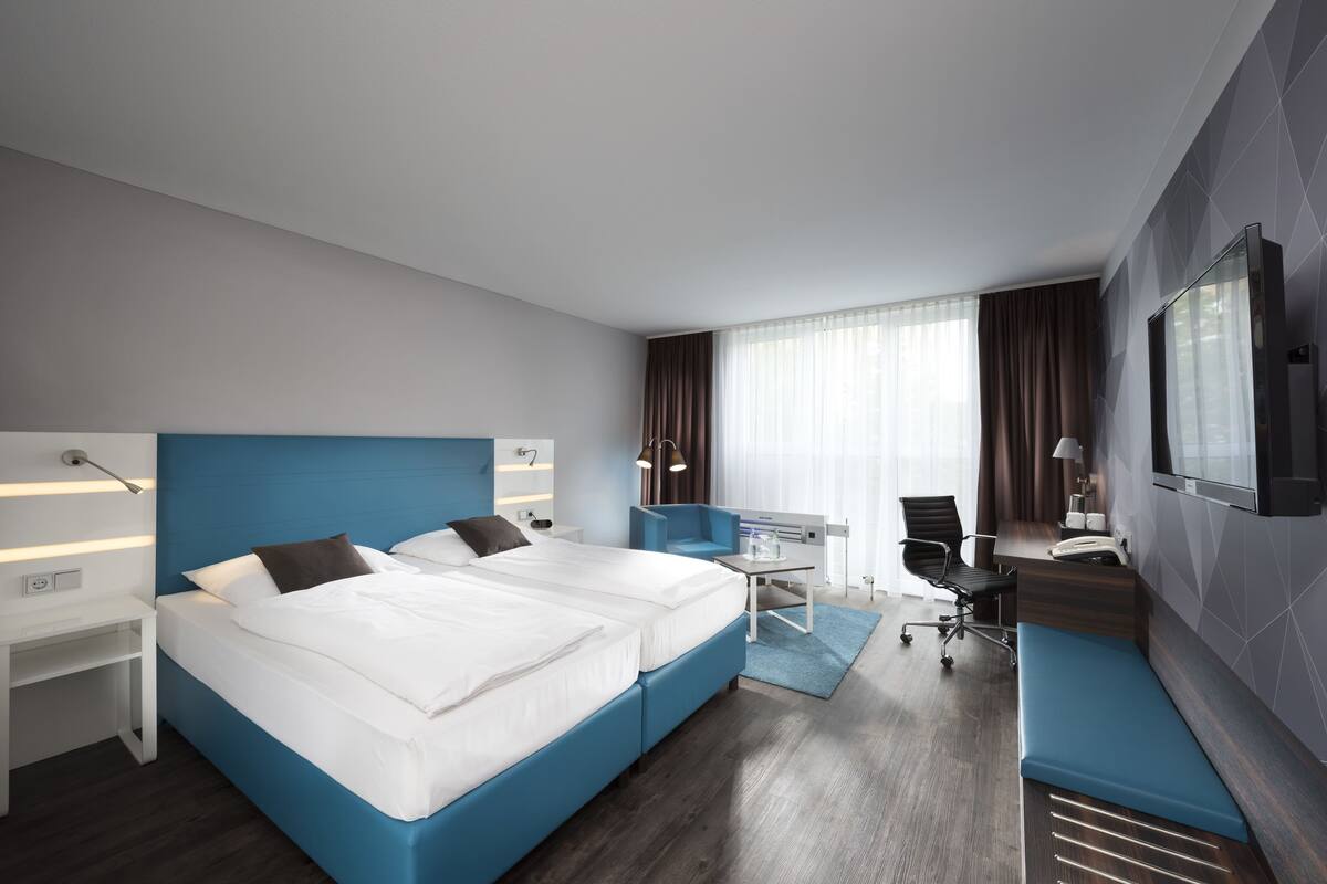 Ein modernes Hotelzimmer mit einem großen Bett, einem Schreibtisch, einem Sessel und einem Fernseher.