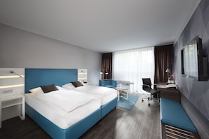 Ett modernt hotellrum med en stor säng, ett skrivbord, en stol och en TV.
