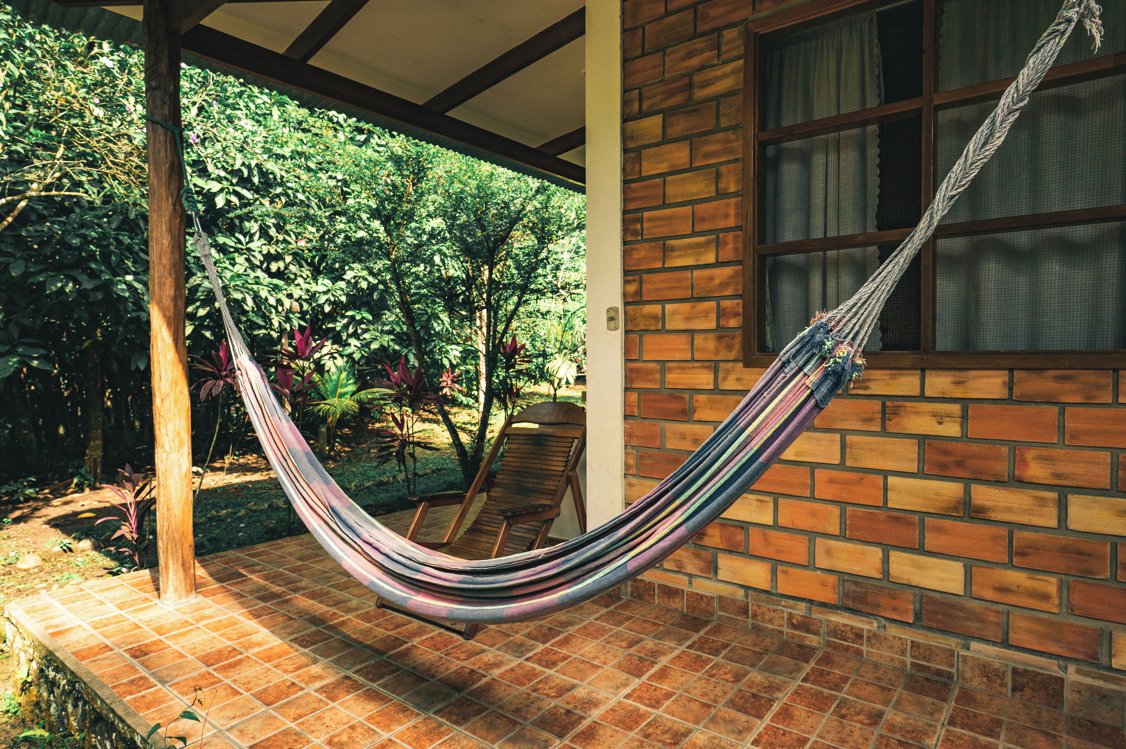 Una hamaca en un patio con baldosas, una pared de ladrillo y una ventana.