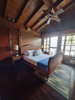 Una habitación de madera con una cama, un ventilador de techo y ventanas grandes.
