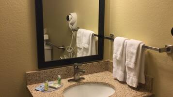 A bathroom with a granite countertop sink, a mirror, a hairdryer, and a towel rack.