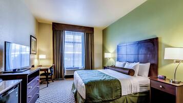 Habitación de hotel con cama, escritorio, silla, televisor y ventana con cortinas.