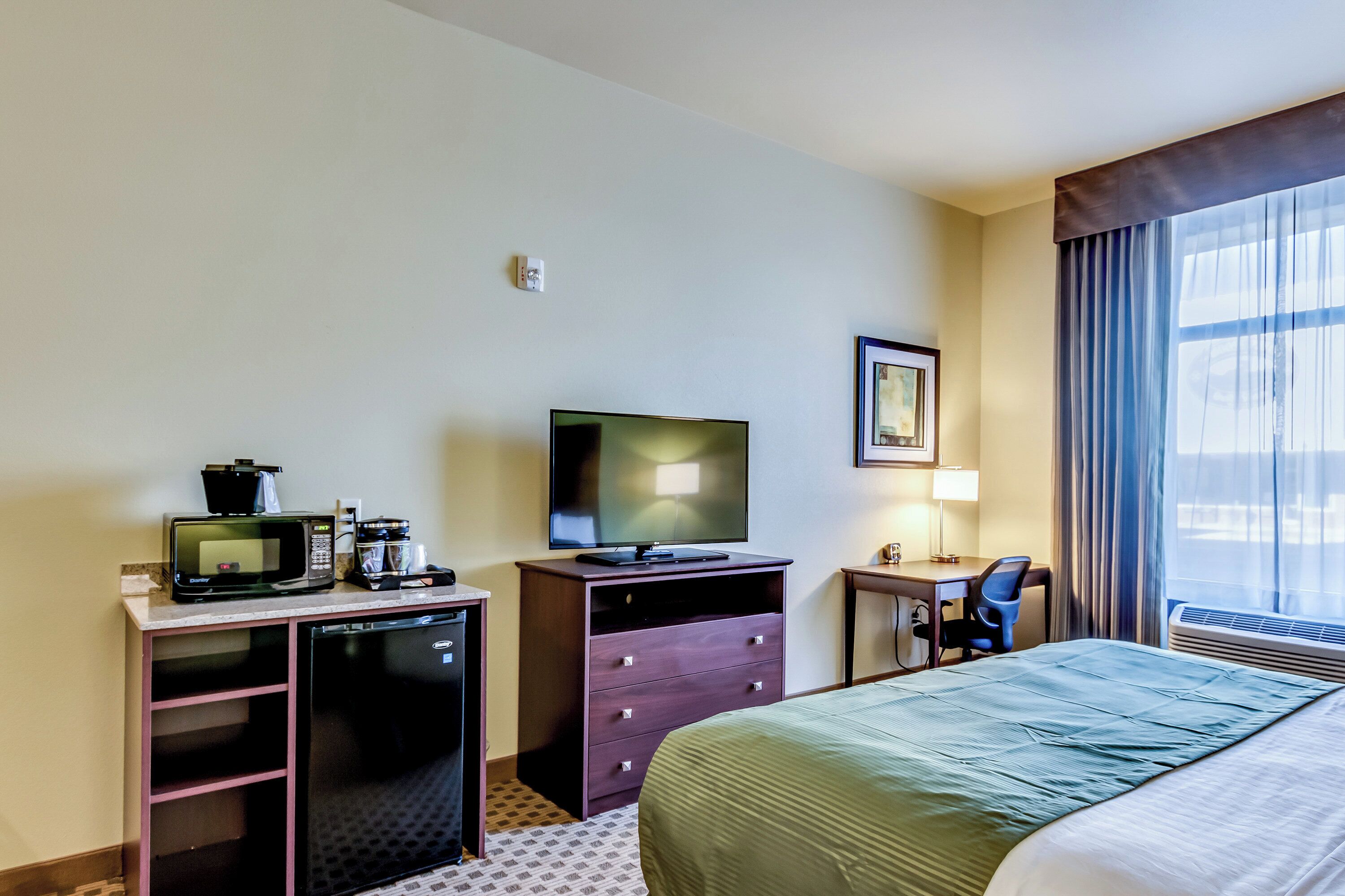 Une chambre d’hôtel équipée d’un lit, d’un bureau avec un ordinateur, d’une télévision, d’un four à micro-ondes et d’une machine à café.