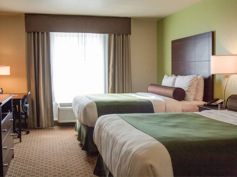 A hotel room with two beds, a desk, a chair, and a lamp.