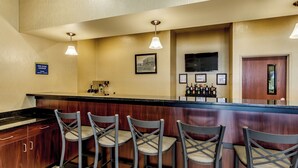 A bar area with wooden bar counter and four bar stools. There are overhead lights, a television, and framed certificates on the wall. - Cobblestone Inn & Suites - Waverly (Waverly)