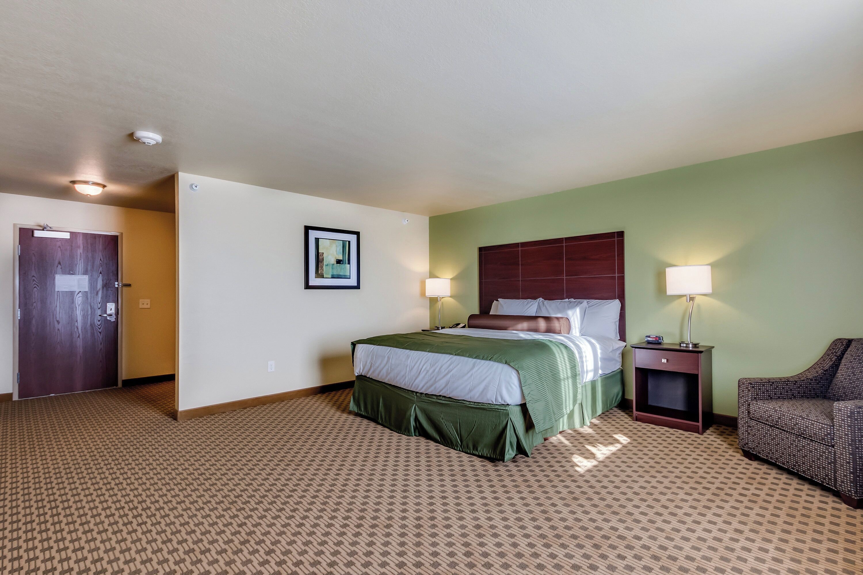 A hotel room with a bed, two bedside lamps, a chair, and a door.