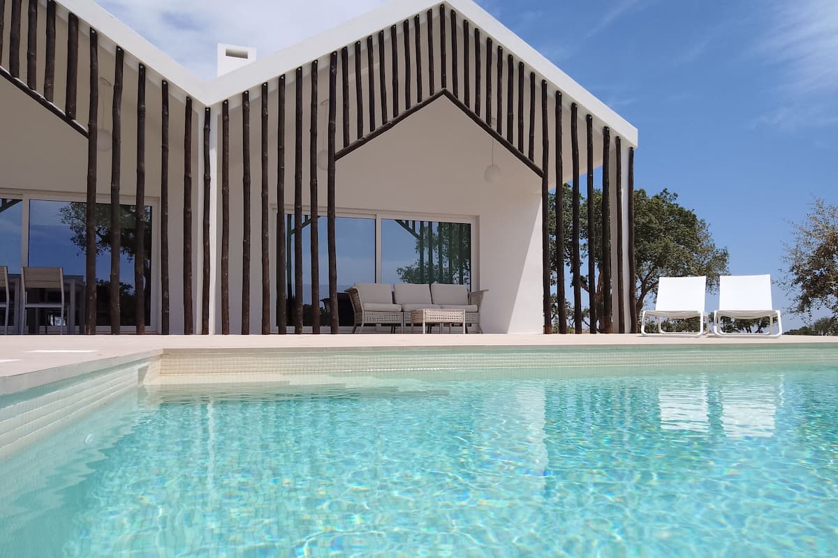 Un edificio moderno con piscina, ventanas amplias y zona de estar al aire libre.