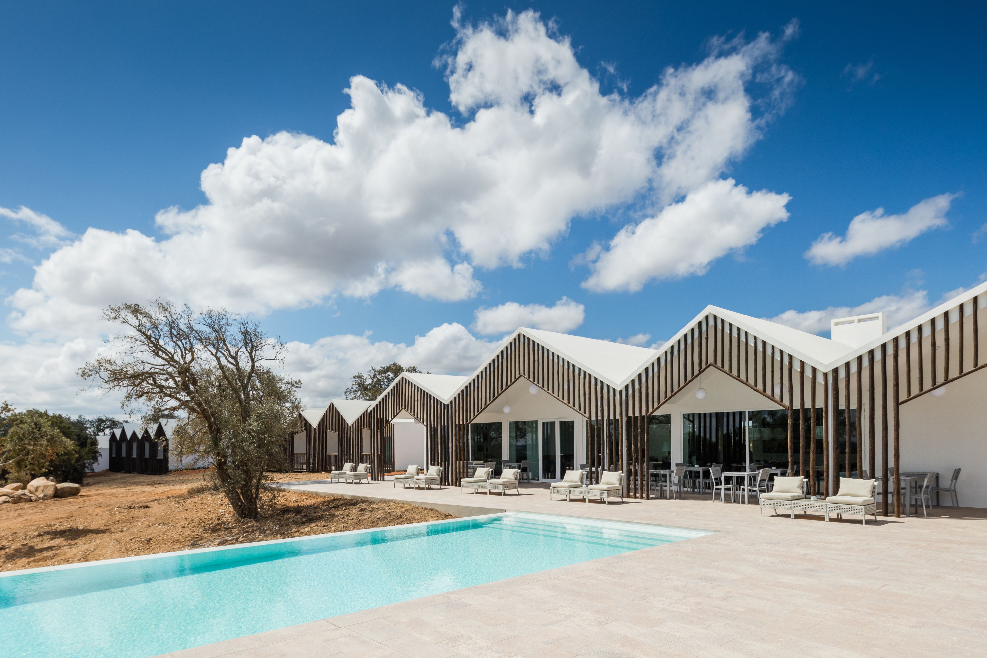 Un hotel moderno con piscina, mobiliario exterior y cielo azul despejado.