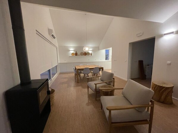Una sala de estar moderna con chimenea, un comedor con mesa y sillas de madera, y una cocina al fondo.