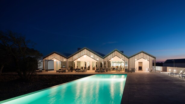 Un hotel moderno con piscina, mobiliario exterior y una fachada bien iluminada.