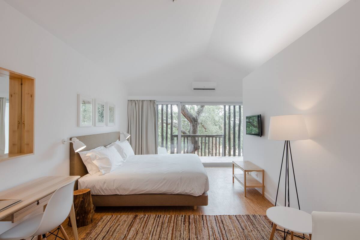 Una habitación de hotel moderna con una cama grande, un escritorio, una silla, una mesita y un televisor.