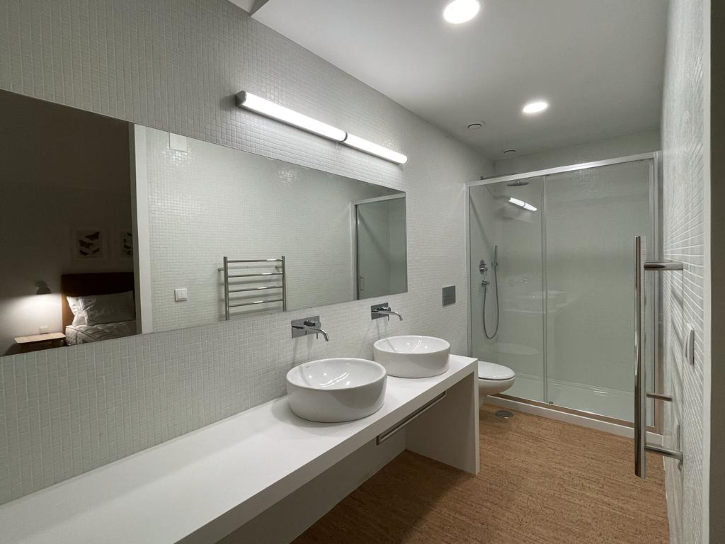 Un baño moderno con un espejo grande, dos lavamanos, ducha e inodoro.