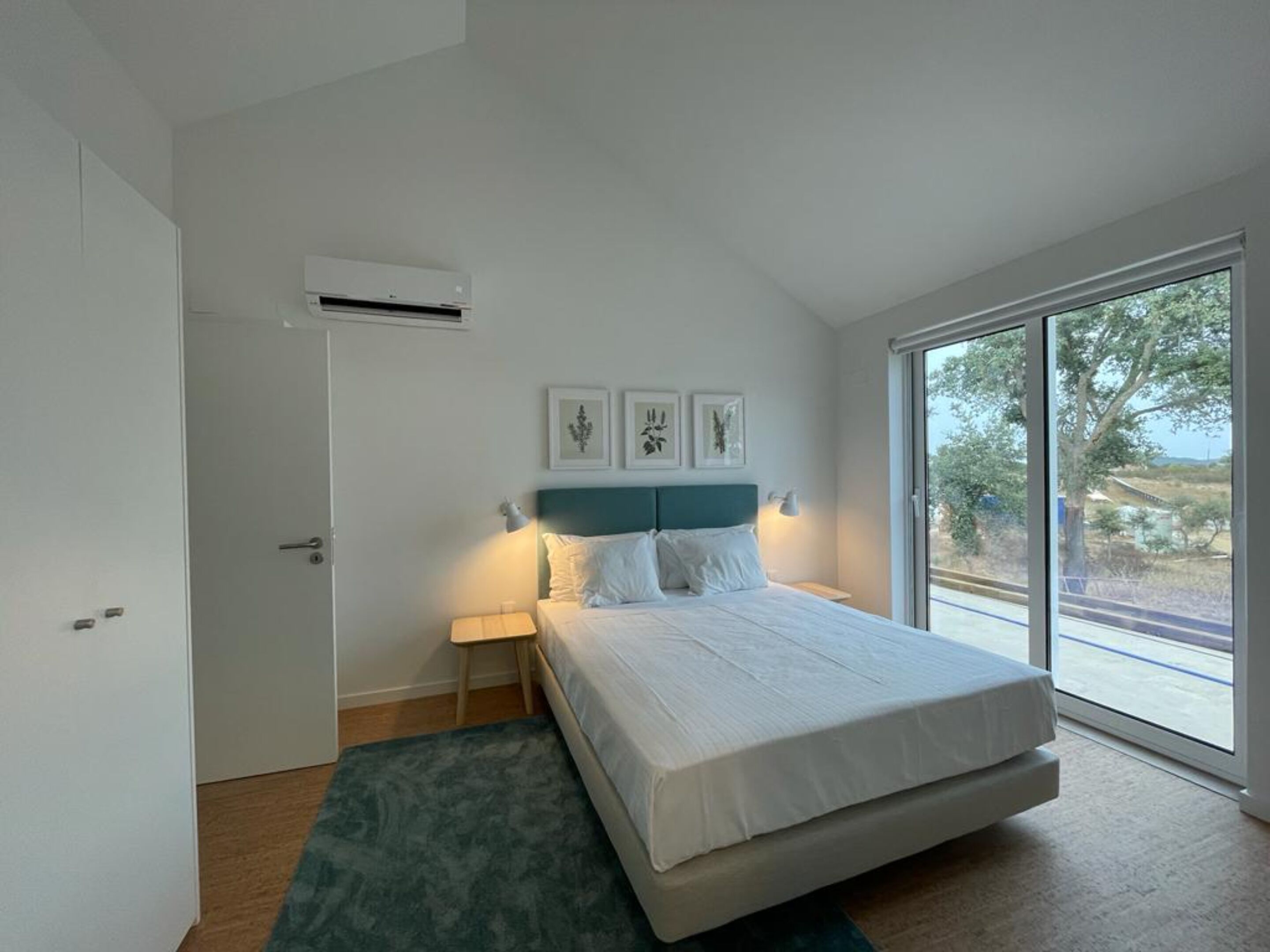 A bedroom with a bed, a nightstand, a lamp, and a window with a view of trees.